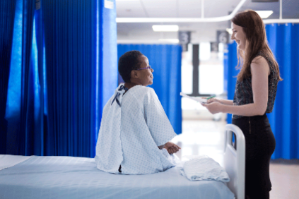 Photo of a pharmacist attending to a hospital patient at their bedside