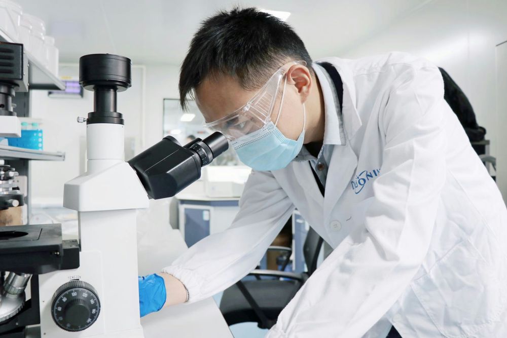 Photo by Kelly Chiang on Unsplash of a man in a lab coat and a face mask looking into a microscope