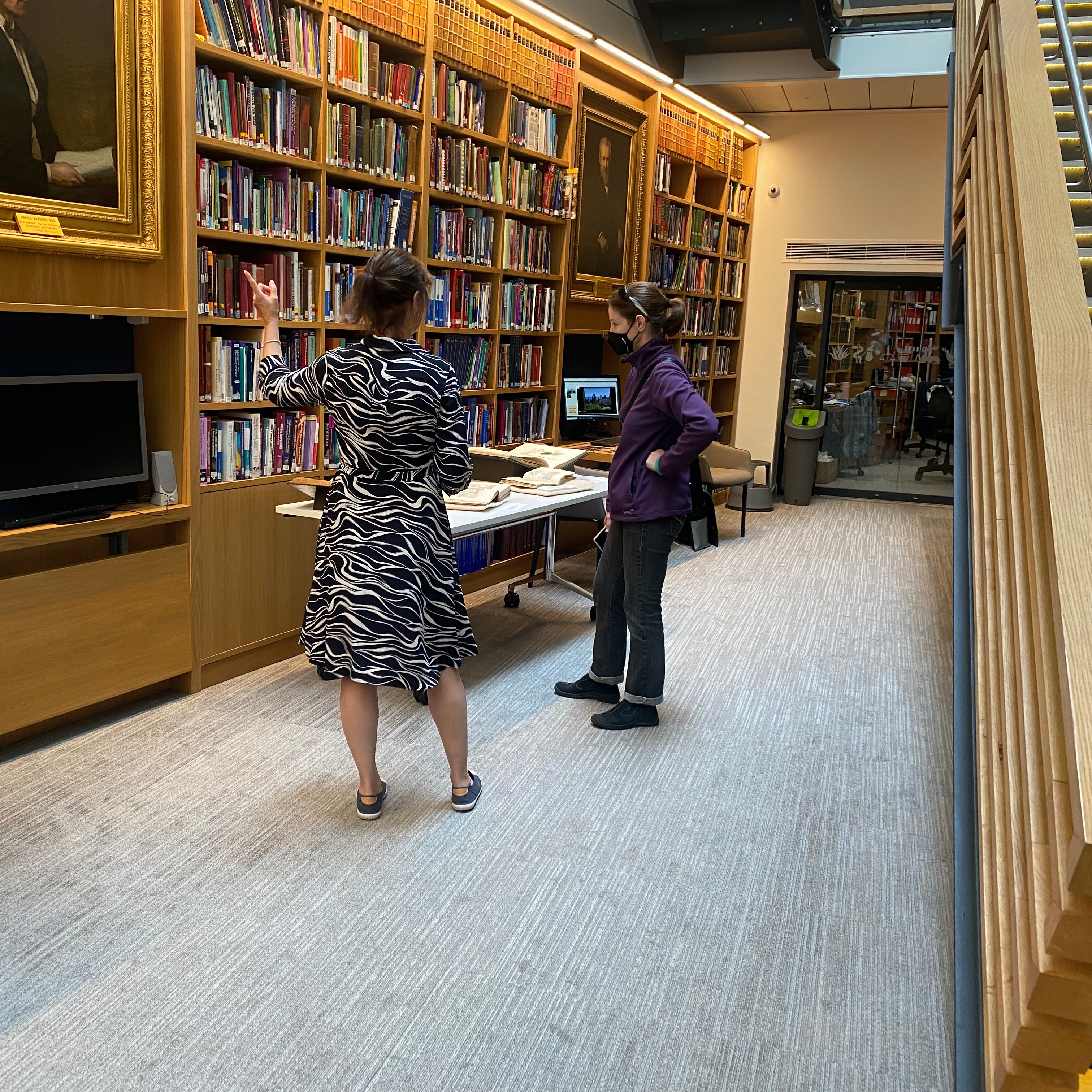 Image of library reading room, with books on shelves and a portrait of Daniel Hanbury, showing Librarian Karen supporting a visitor.